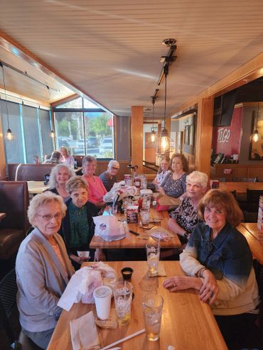 A group of elderly women gathered around a restaurant table, smiling and enjoying their time.