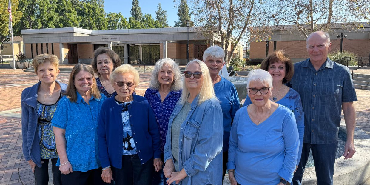 Group of seniors posing outdoors in front of a community building on a sunny day.