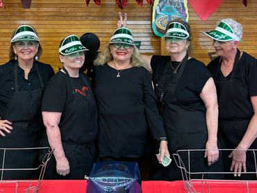 Group of five women wearing Las Vegas visors and black aprons, smiling and posing playfully indoors.