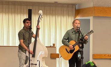 Two musicians perform with a white double bass and an acoustic guitar indoors.