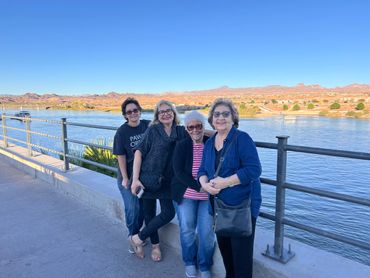 Four women smiling by a river with mountains in the background.