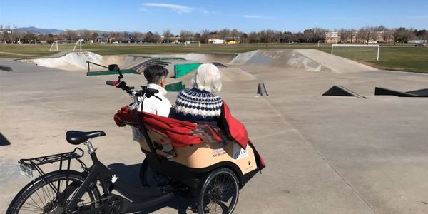 Two people seated on a bike rickshaw at a skatepark on a sunny day.