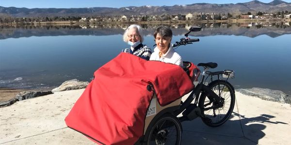 Two elderly women with a bike by a lake on a sunny day.
