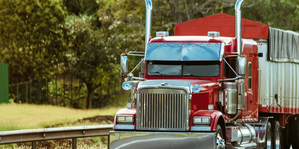 Red semi-truck driving on a highway surrounded by greenery.