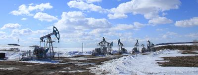 Oil pump jacks in a snowy field under a blue sky.