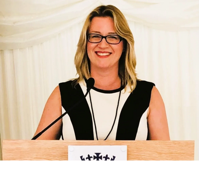 A smiling woman with glasses at a podium with a microphone.