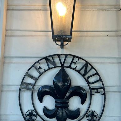 A lit lantern above a 'BIENVENUE' metal sign with a fleur-de-lis.