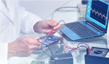 Technician testing electronic circuit connected to laptop displaying waveform.