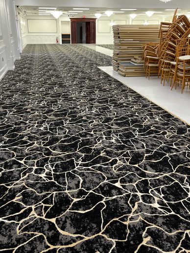 Stacked chairs and tables in a spacious, elegant room with patterned carpet.