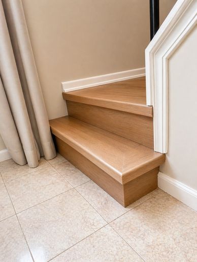 Close-up of wooden stairs with tiled floor and beige curtains.