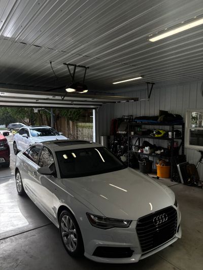 White Audi sedan parked inside a garage with tools and equipment in the background.