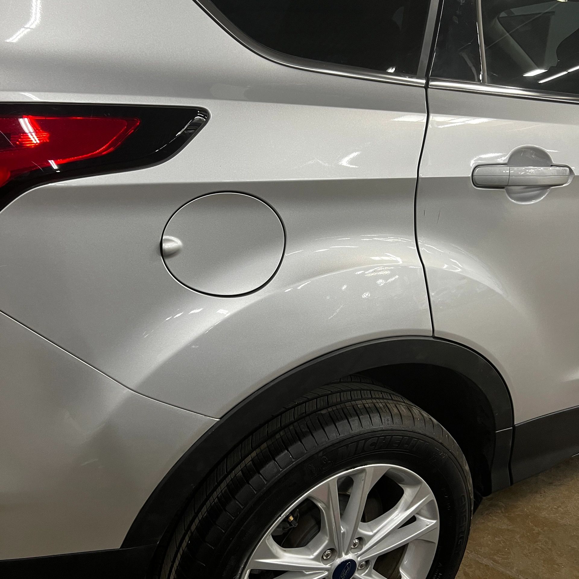 Close-up of a silver car's rear side with wheel and fuel cap.