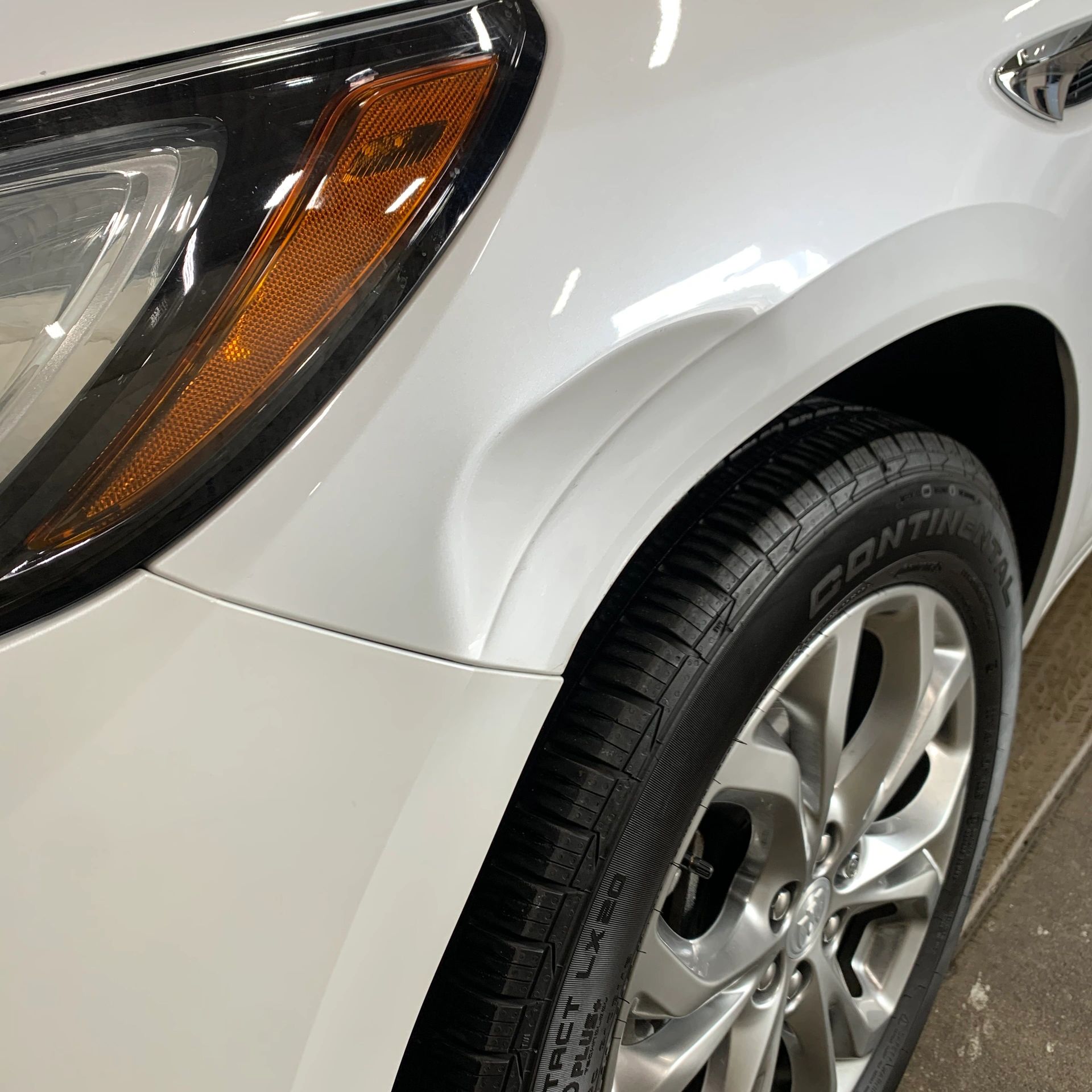 Close-up of a white car's front wheel and headlight area.