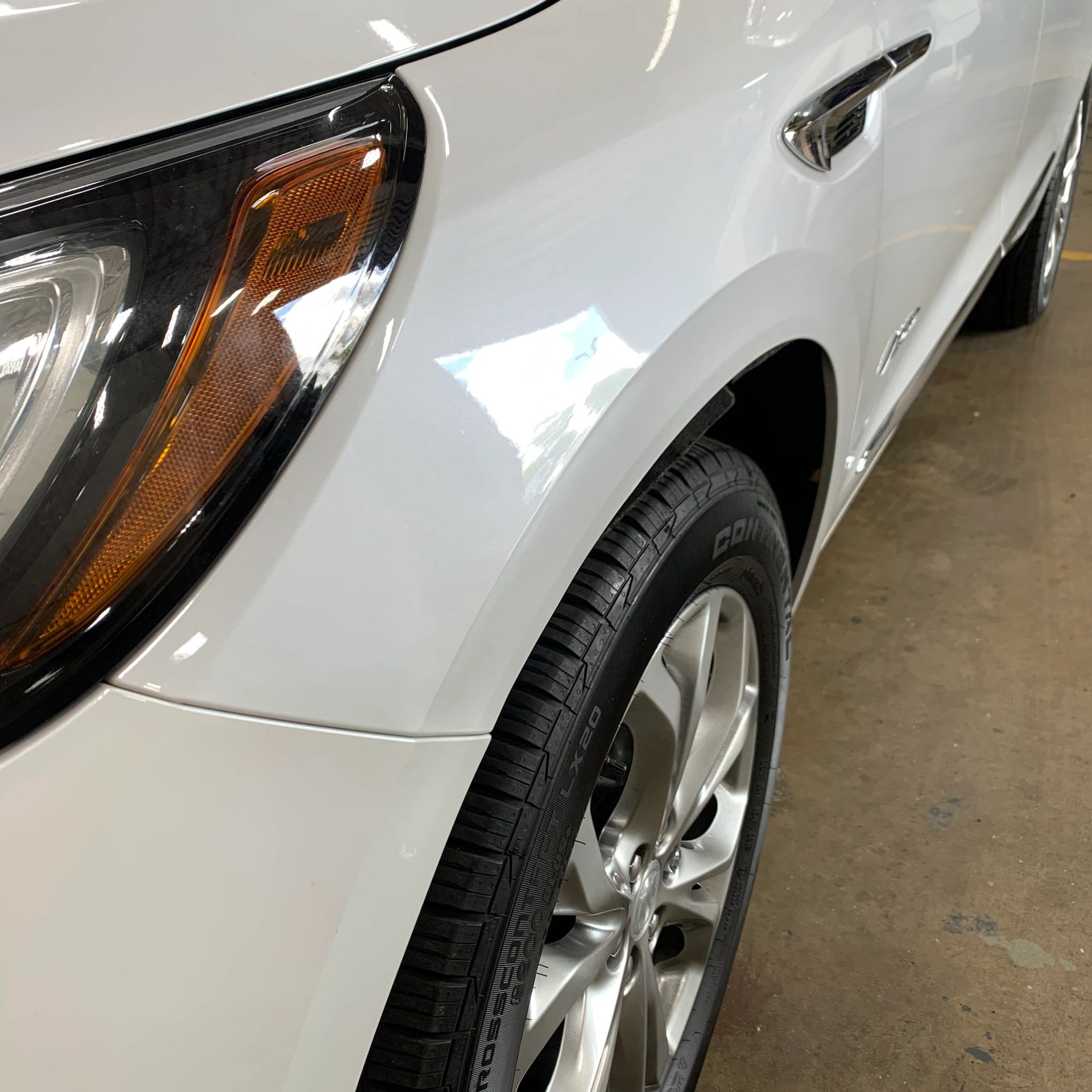 Close-up of a white car's front side, showing the headlight, tire, and part of the door.