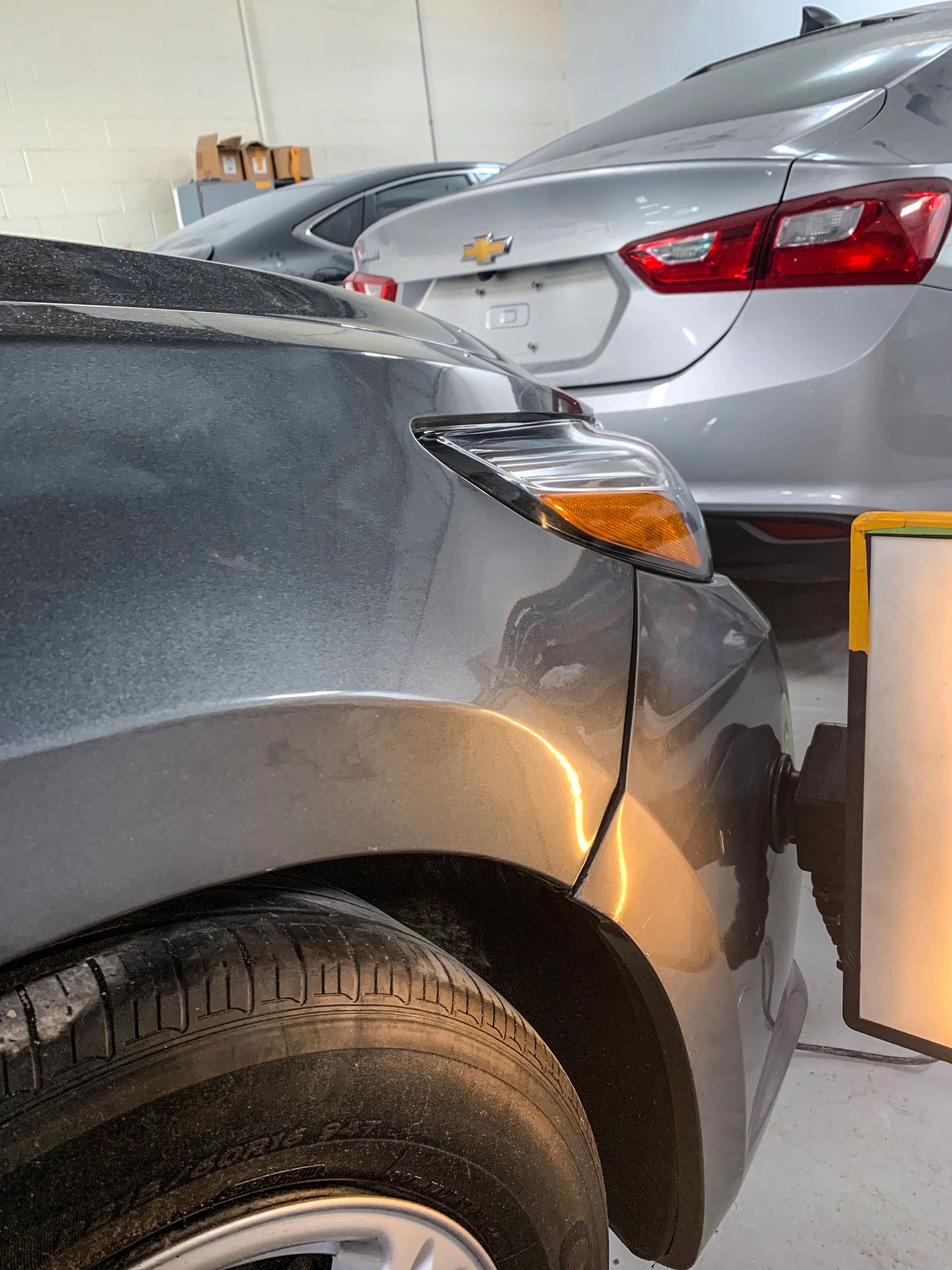 Close-up of two parked cars in a garage with a reflection light on one car.