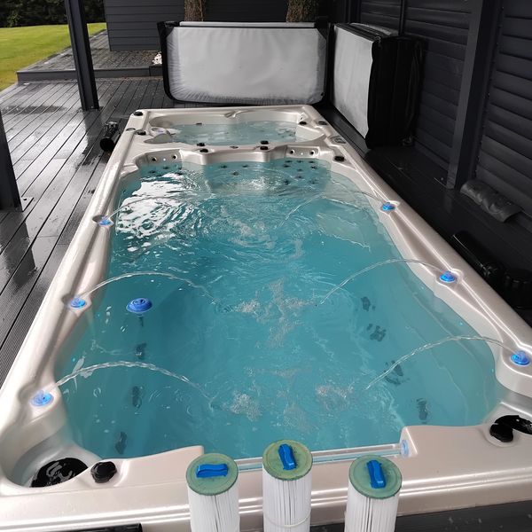 Large outdoor hot tub with clear blue water and jets on a wooden deck.