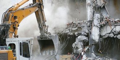 Hydraulic excavator tearing down concrete building using demolition contractor insurance. Contractor