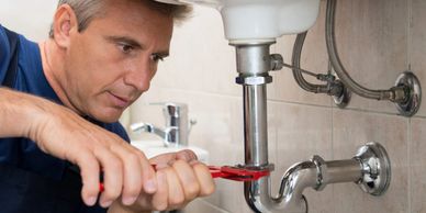 Plumber under sink working on leaking pipe while properly insured with plumber insurance.