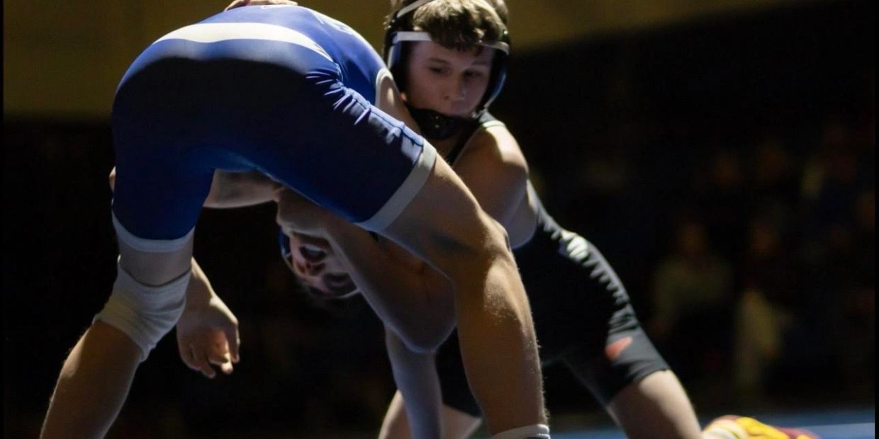 Two wrestlers engaged in a match under spotlight lighting.