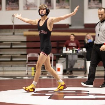 Young wrestler celebrating victory on the mat with arms outstretched.