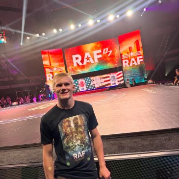 Smiling young man in RAF t-shirt at an illuminated event stage.