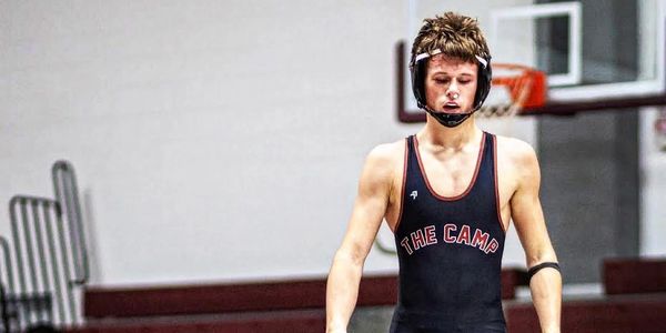 Young wrestler in black singlet preparing for a match in a gym.