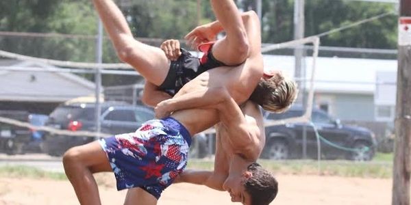Two young men wrestling outdoors on a sandy surface.