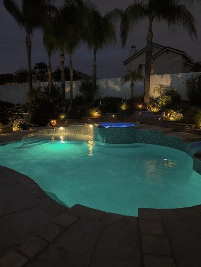 A serene backyard pool illuminated at night with palm trees and ambient lighting.