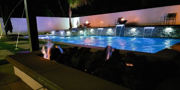 Pool and fire pit at night with laminated water descents and low voltage lighting