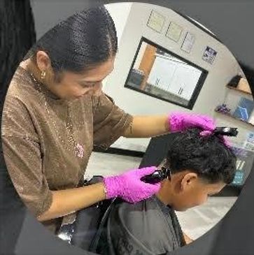 A hairdresser wearing pink gloves cuts a boy's hair in a salon.