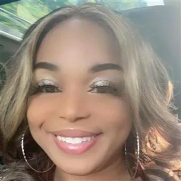 A smiling woman with hoop earrings and shimmery eye makeup.