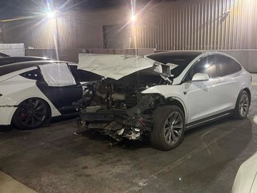 Damaged white Tesla Model X with front end smashed pending repair assessment.