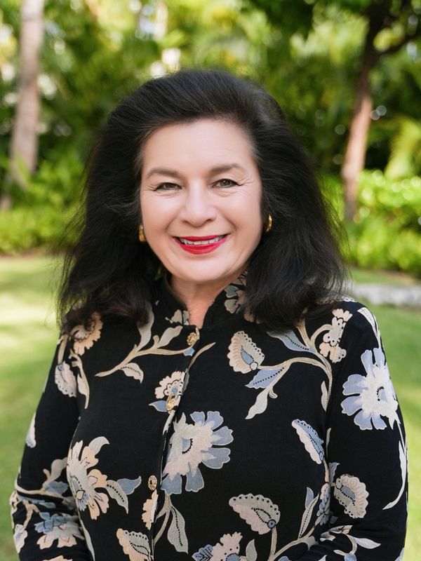 Smiling woman in a floral black blouse outdoors.