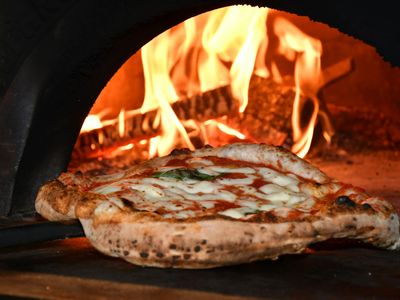 A pizza baking inside a wood-fired oven with flames.