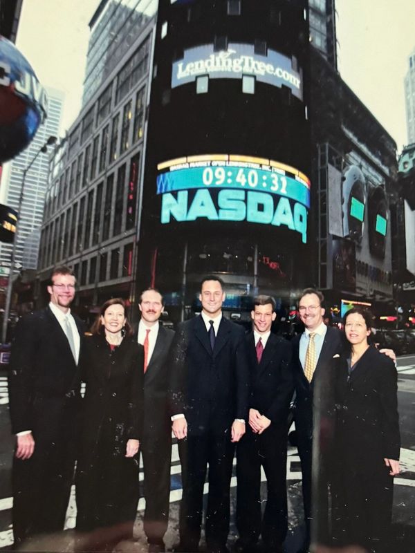 Group of professionals posing in front of a NASDAQ sign.