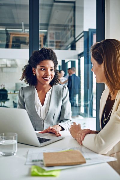 Two professionals engage in a discussion over a laptop, with documents and a glass of water