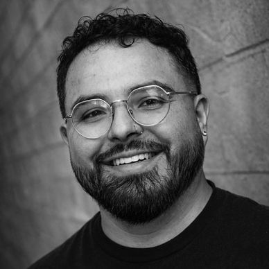 Smiling man with glasses and beard against a textured wall.