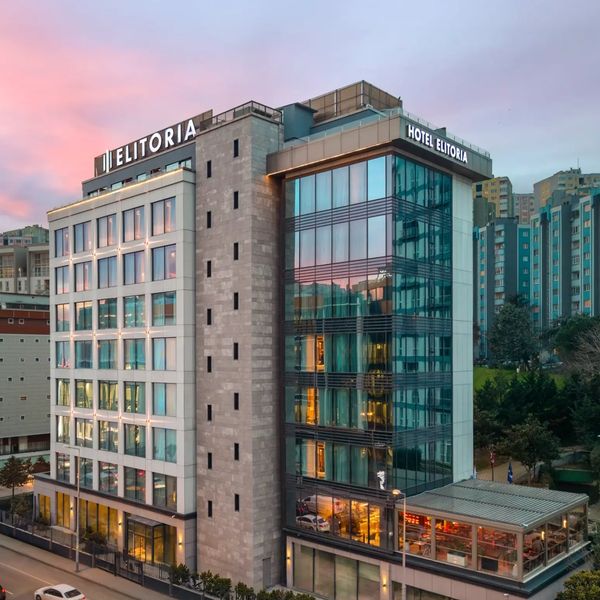 Modern Elitoria Hotel with glass facade at sunset beside busy road.