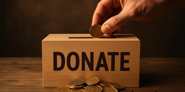 Hand placing coin into a wooden donation box labeled 'DONATE'.