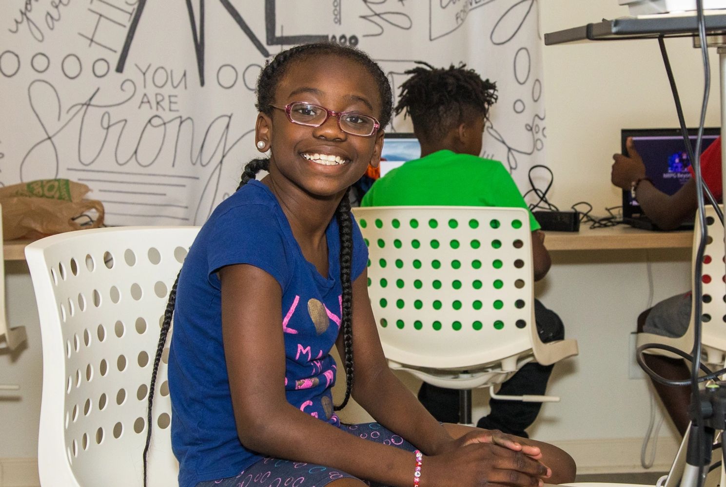 A young girl smiling at the camera and working on a laptop in the community center