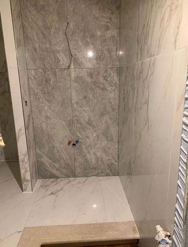 Marble-tiled bathroom corner under construction with plumbing fittings.