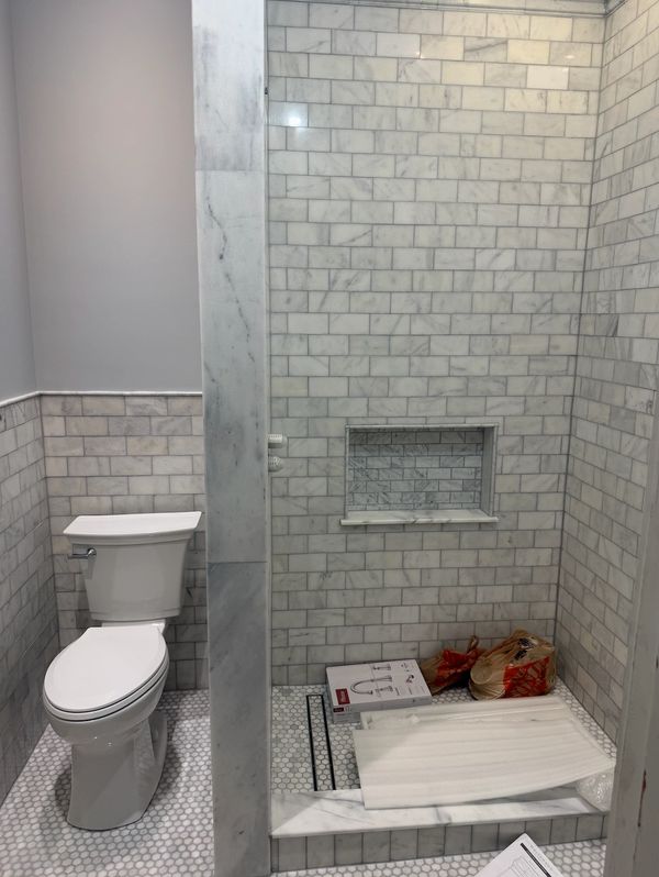 Newly tiled bathroom with a white toilet and a walk-in shower under construction.