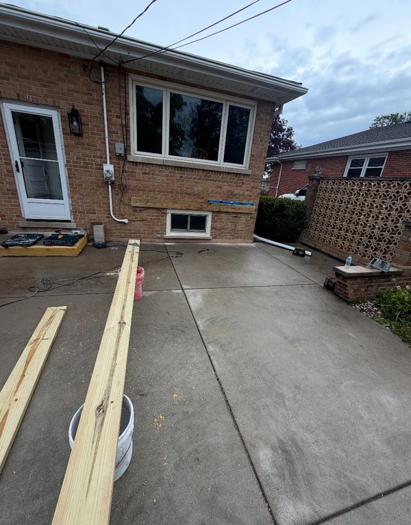 Construction materials and tools on a concrete patio outside a brick house.
