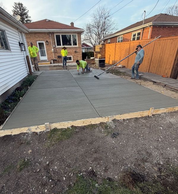 Workers finishing a freshly poured concrete patio in a backyard.