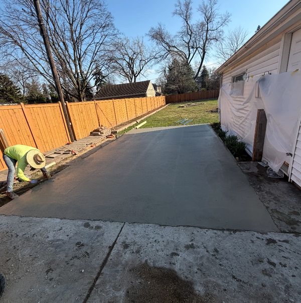 Worker smoothing freshly poured concrete slab in a backyard.