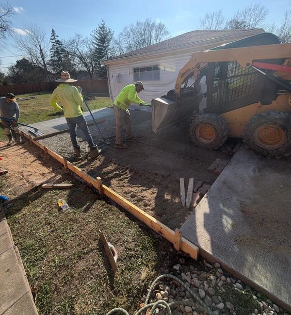 Workers using machinery to lay concrete near a house on a sunny day.