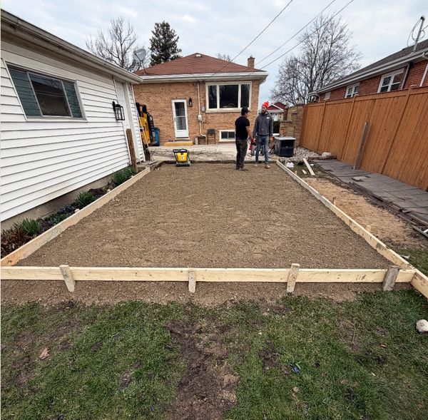 Two men discussing a freshly prepared rectangular dirt foundation in a backyard.