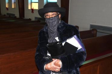 Person in a dark coat and hat sitting inside a church.