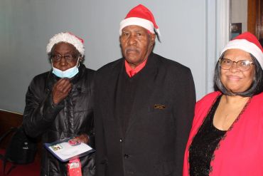 Three people wearing Santa hats posing indoors during a festive event.
