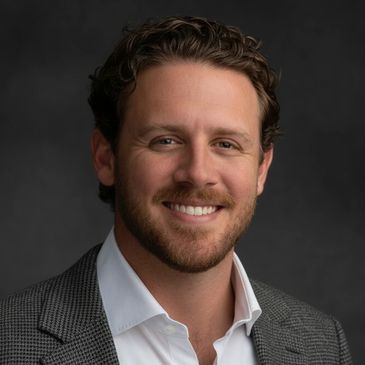 Smiling man in blazer with dark background.